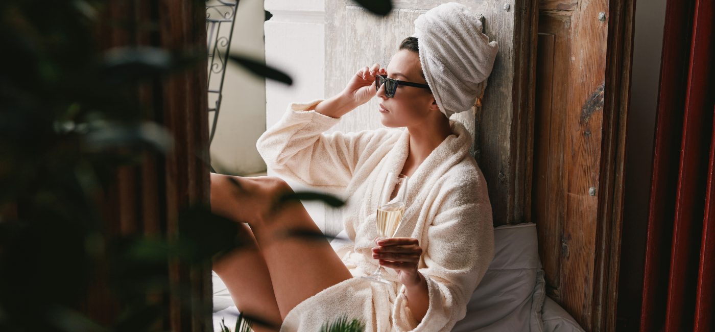 Beautiful young woman in bathrobe enjoying champagne while relaxing on the balcony
